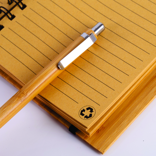 Caderno em capa de bambu com elástico, suporte para caneta e com 70 folhas pautadas. 18 x 13,5 cm. Acompanha caneta de bambu com detalhes em plástico.